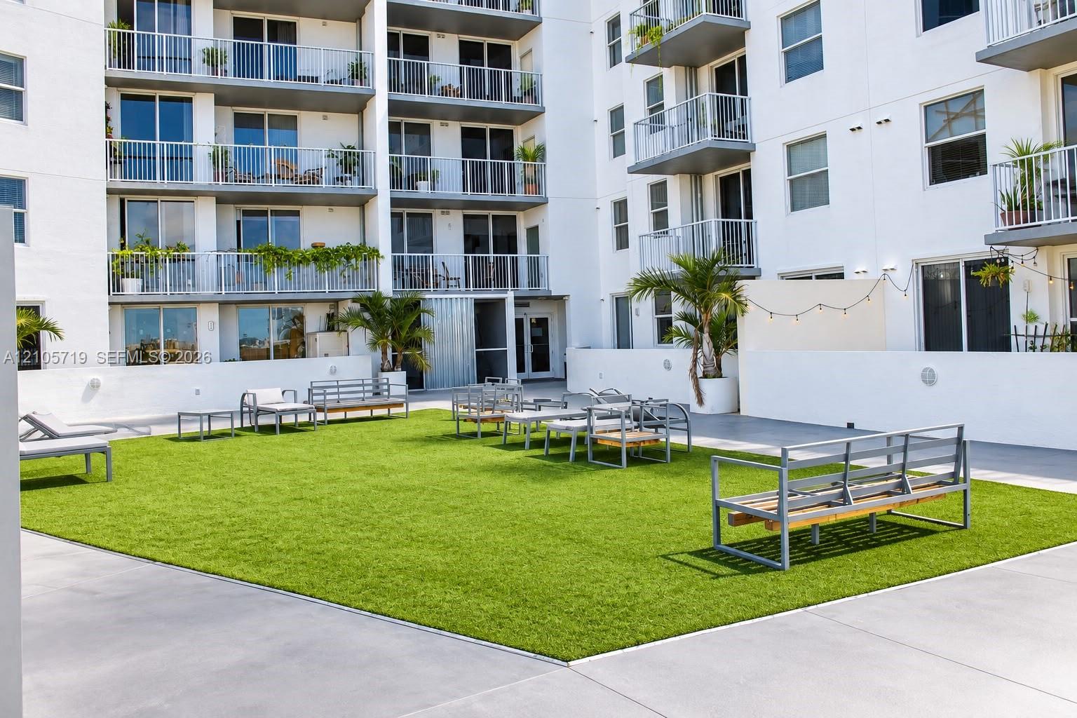 Outdoor courtyard featuring a manicured lawn, smooth concrete perimeter, perimeter wall lighting, and established palm trees