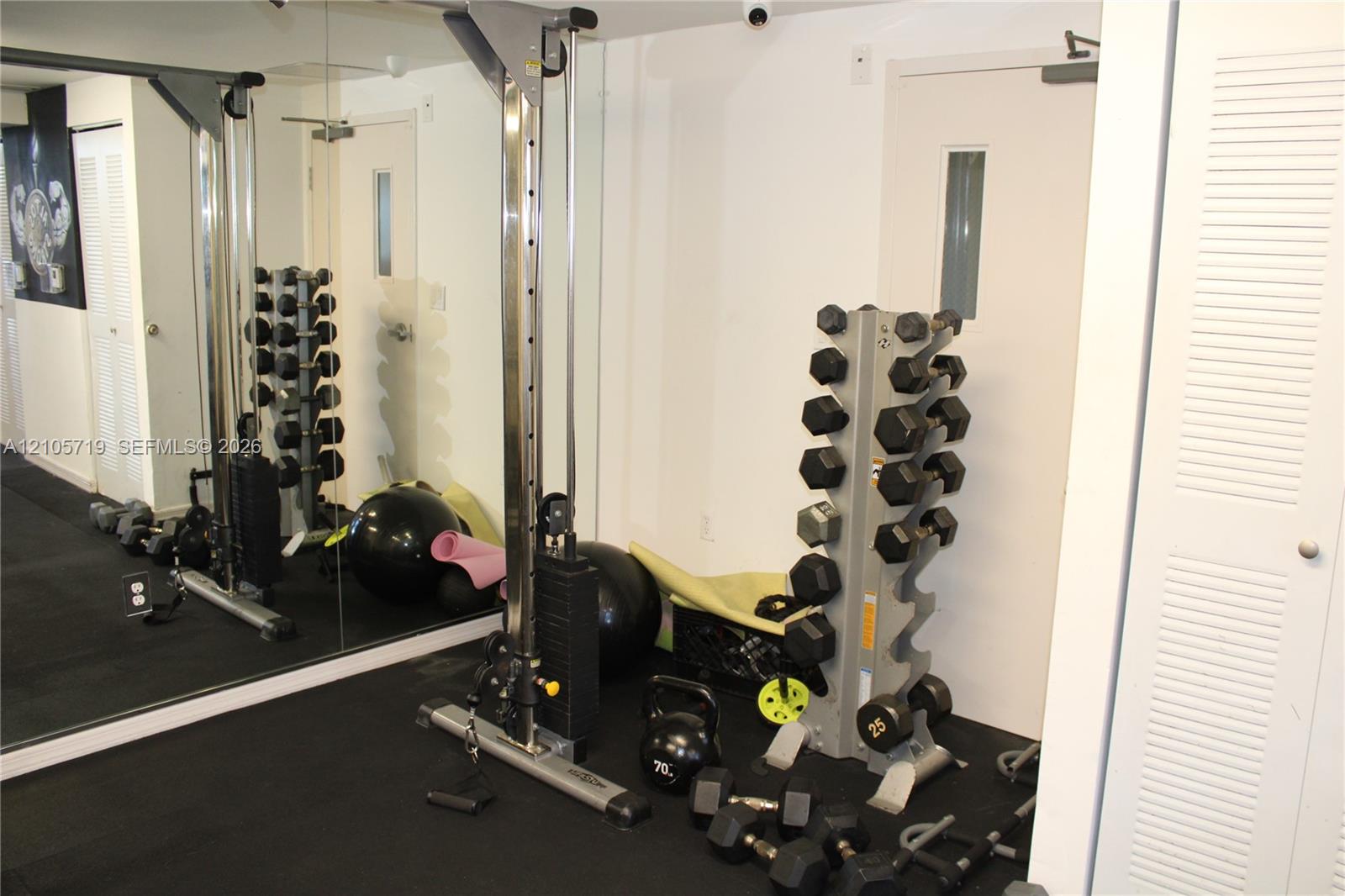 Full-wall mirror, solid rubber flooring, and louvered-panel closet doors