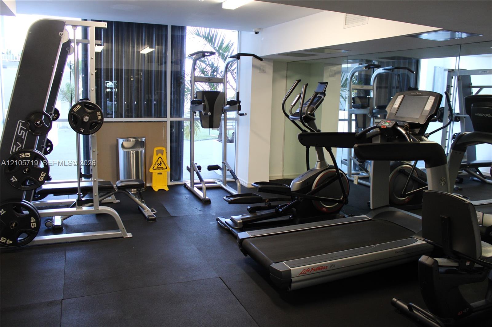 Fitness center featuring floor-to-ceiling windows, mirrored walls, and rubberized flooring