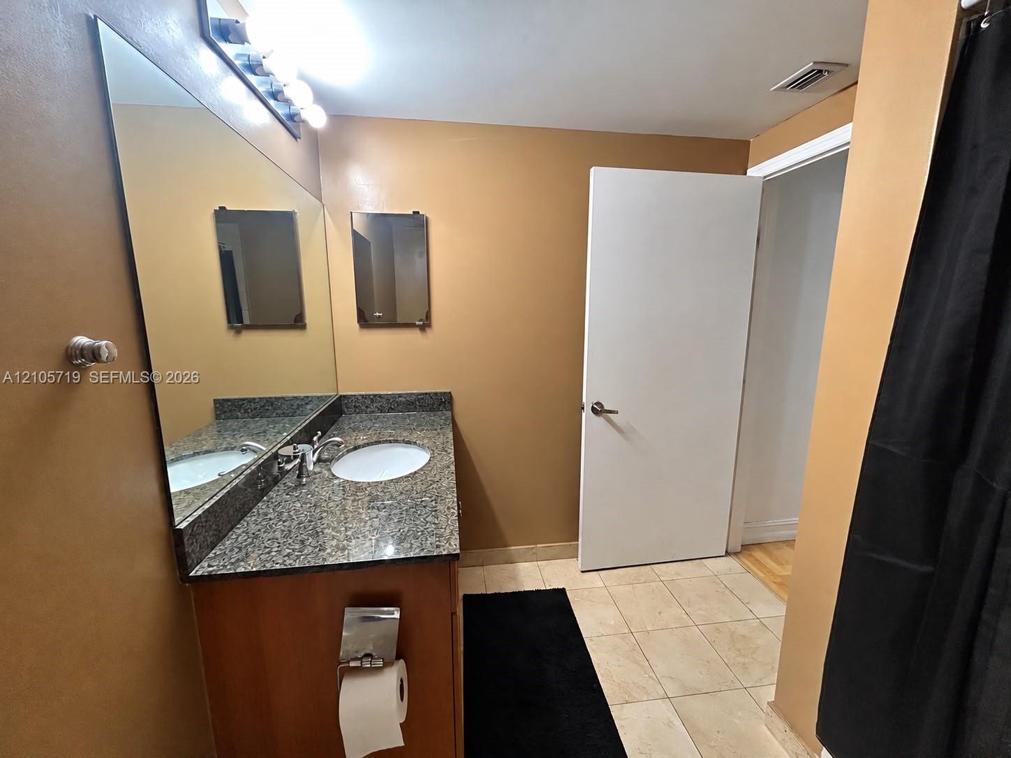 Vanity featuring stone-style countertop, oval undermount sink, large wall-mounted mirror, and tile flooring