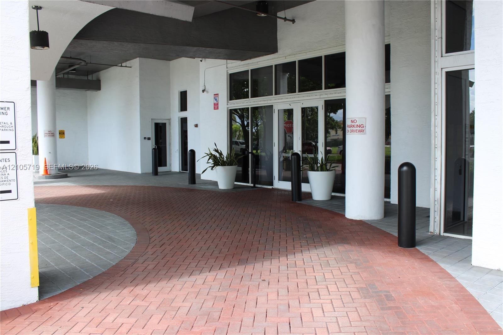 Covered drive-up entrance featuring a herringbone brick paver motor court, structural cylindrical columns, and expansive glass-paneled double entry doors