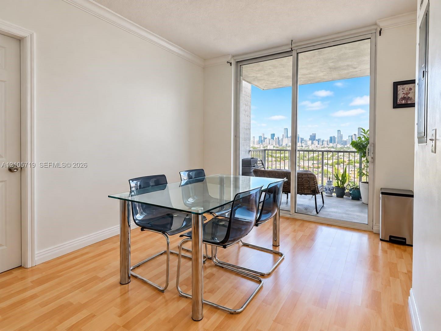 Living area featuring wood-finish flooring, crown molding, and large sliding glass doors leading to a private balcony with cityscape scenery