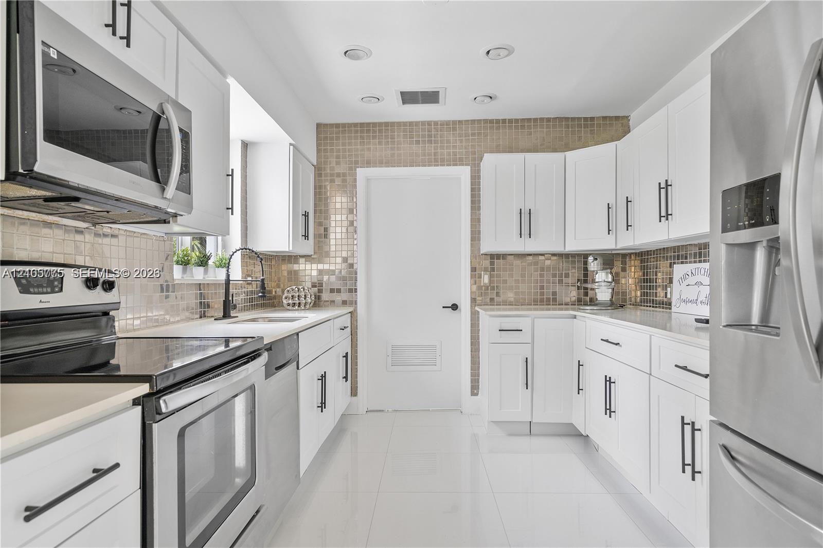 Kitchen featuring white cabinetry with matte black hardware, stainless steel appliances, a metallic mosaic tile backsplash, and gloss-finish floor tiling