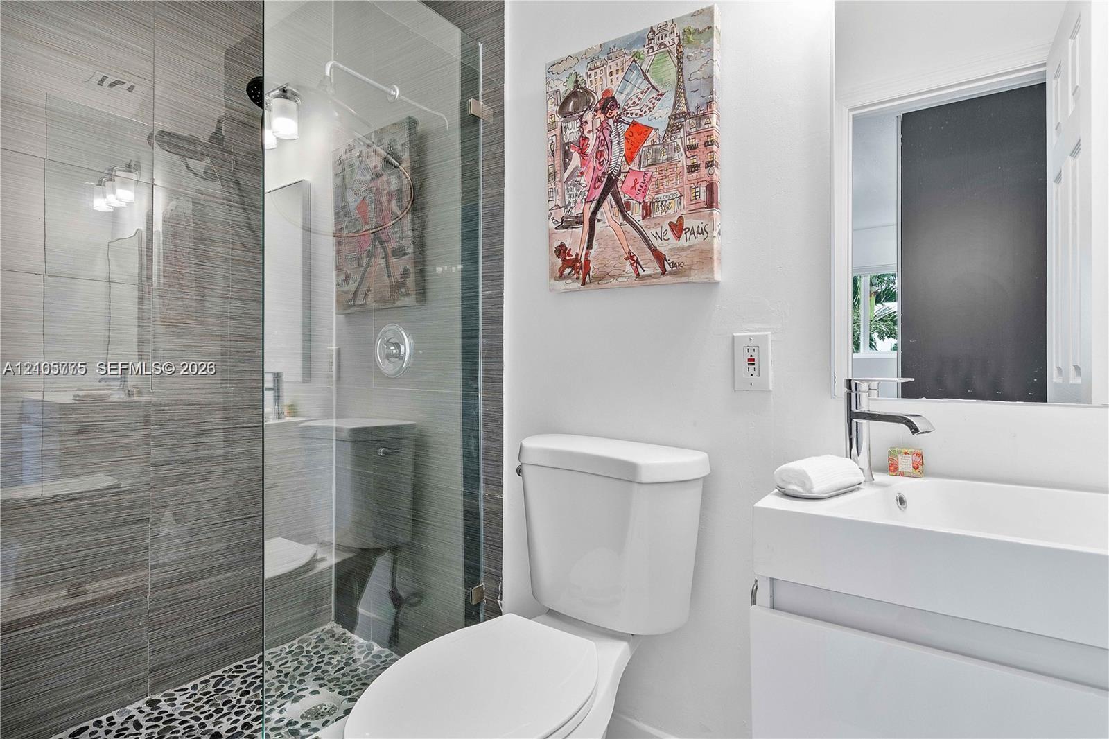 Bathroom featuring a frameless glass walk-in shower with horizontal tile surround and pebble tile flooring, white vanity with a rectangular integrated sink, and polished chrome fixtures