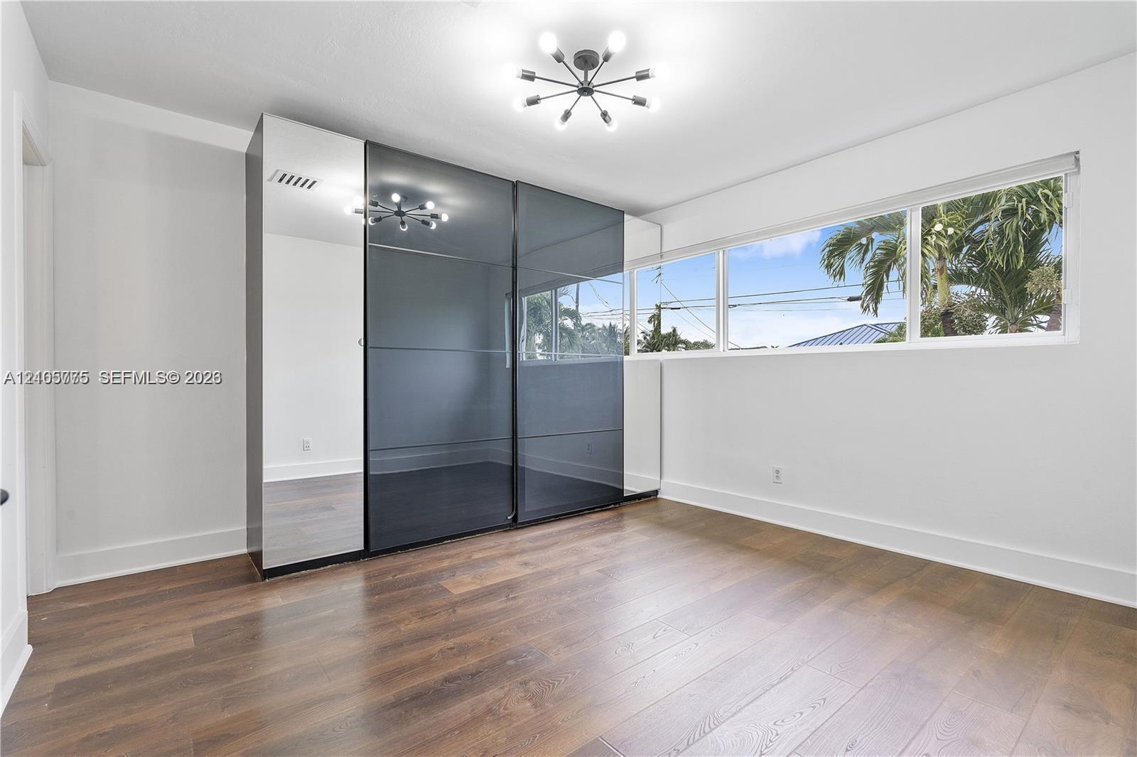 Room featuring wood-finish flooring, large multi-pane horizontal window, modern sputnik-style ceiling light, and full-height built-in wardrobe with mirrored and dark-tinted glass sliding doors