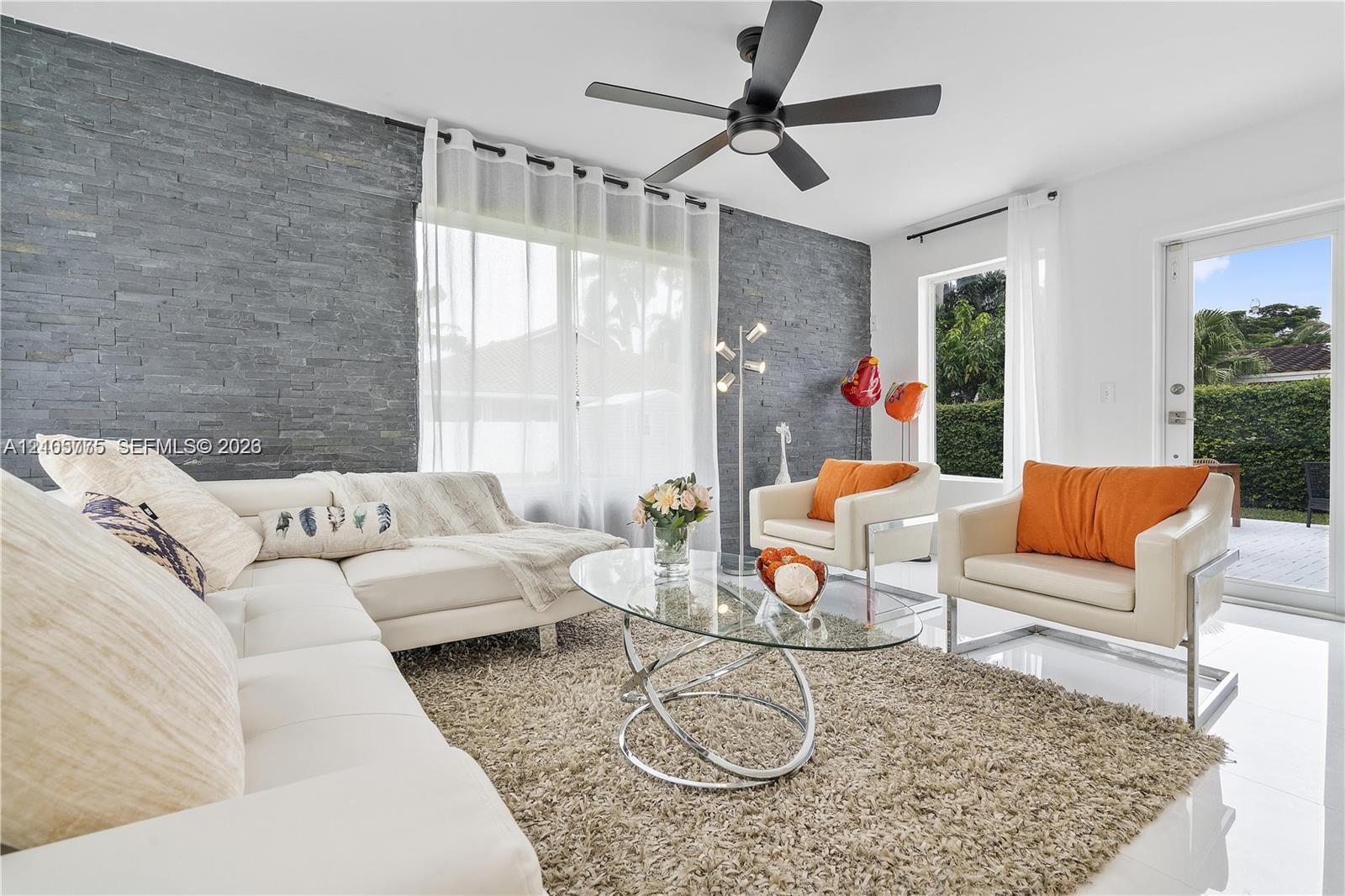 Living space featuring a charcoal-toned stacked stone accent wall, large-format tile flooring, and a modern matte black ceiling fan