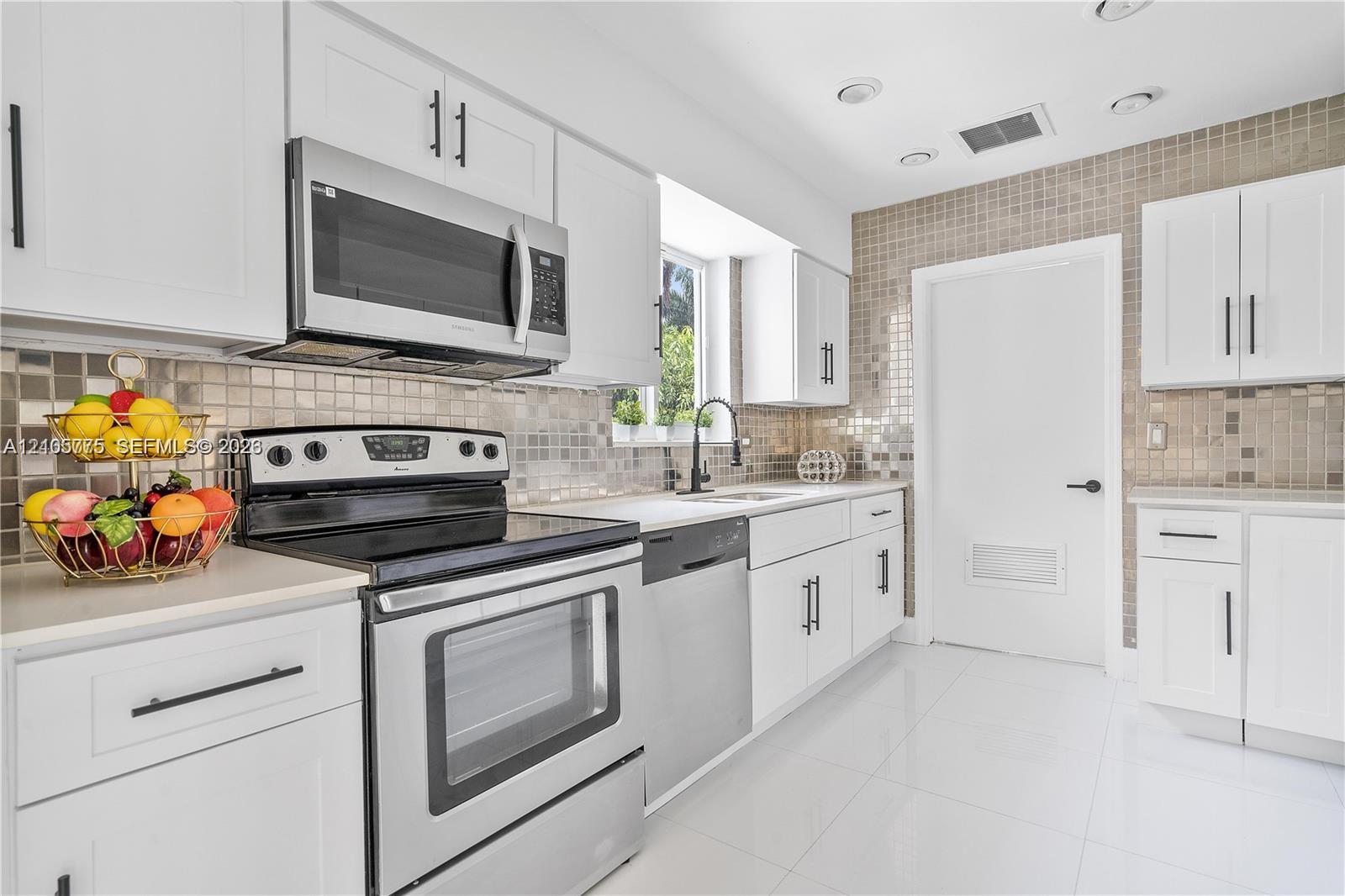 Kitchen featuring white Shaker-style cabinetry, stainless steel appliances, a metallic mosaic tile backsplash, matte black hardware, and tile flooring