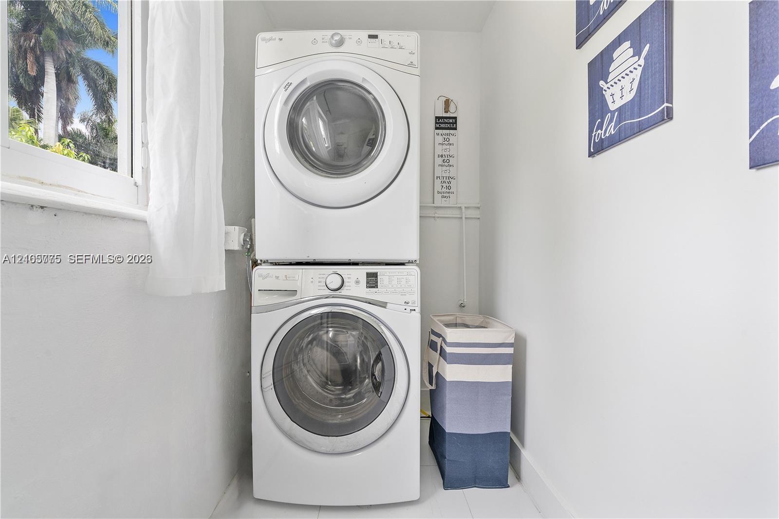 Dedicated laundry area featuring a white stackable front-load washer and dryer set and a window providing natural light