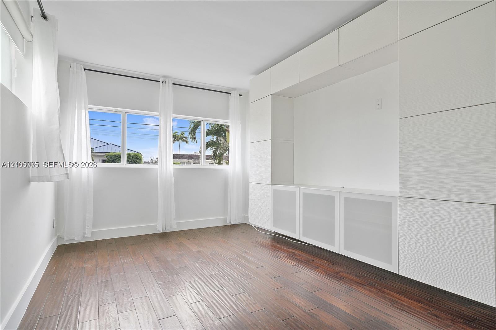 Room with wood-finish flooring, extensive floor-to-ceiling built-in cabinetry, and large windows