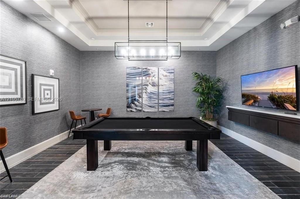Tray ceiling with recessed lighting, textured wall finishes, dark-toned flooring, linear pendant fixture, and wall-mounted cabinetry