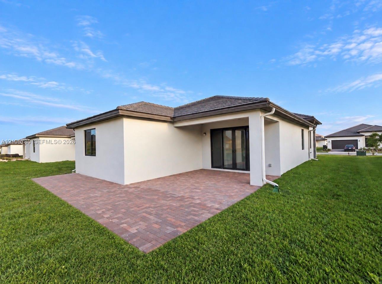 Rear exterior featuring a covered patio with paver hardscaping, light-toned stucco facade, and dark-framed glass doors