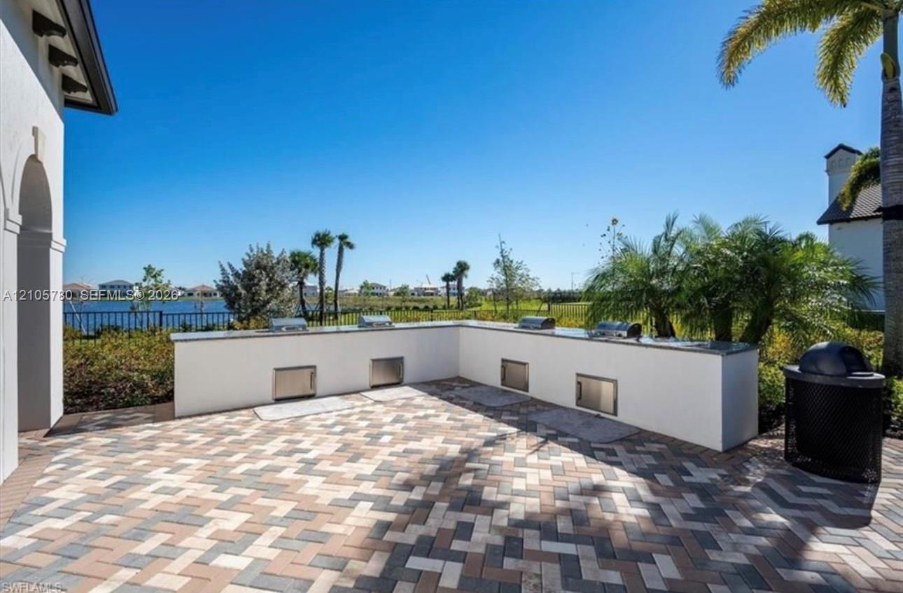 Outdoor kitchen featuring a stone-topped L-shaped island, stainless steel built-in cabinetry, and integrated grill components set on a herringbone-patterned paved patio