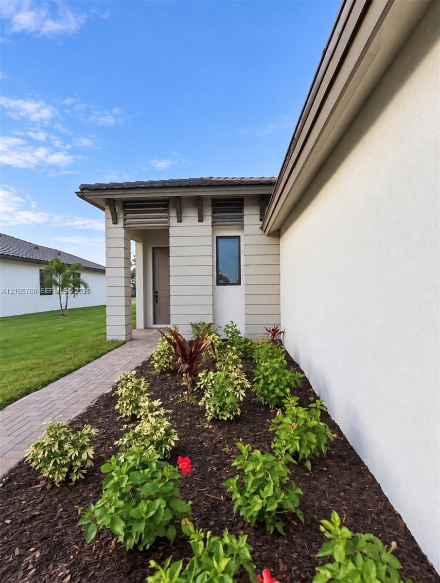 Stucco exterior featuring horizontal siding accents, dark-framed clerestory windows, a paver walkway, and landscaped garden beds with decorative mulch