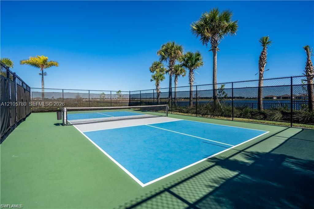 Pickleball court featuring a multi-toned hard surface, mesh perimeter fencing, and mature palm trees