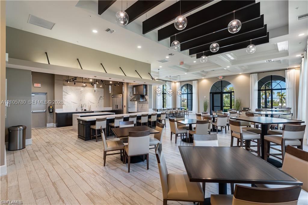 Expansive interior space featuring wood-finish flooring, a coffered ceiling with suspended black structural beams, integrated globe pendant lighting, and arched window frames