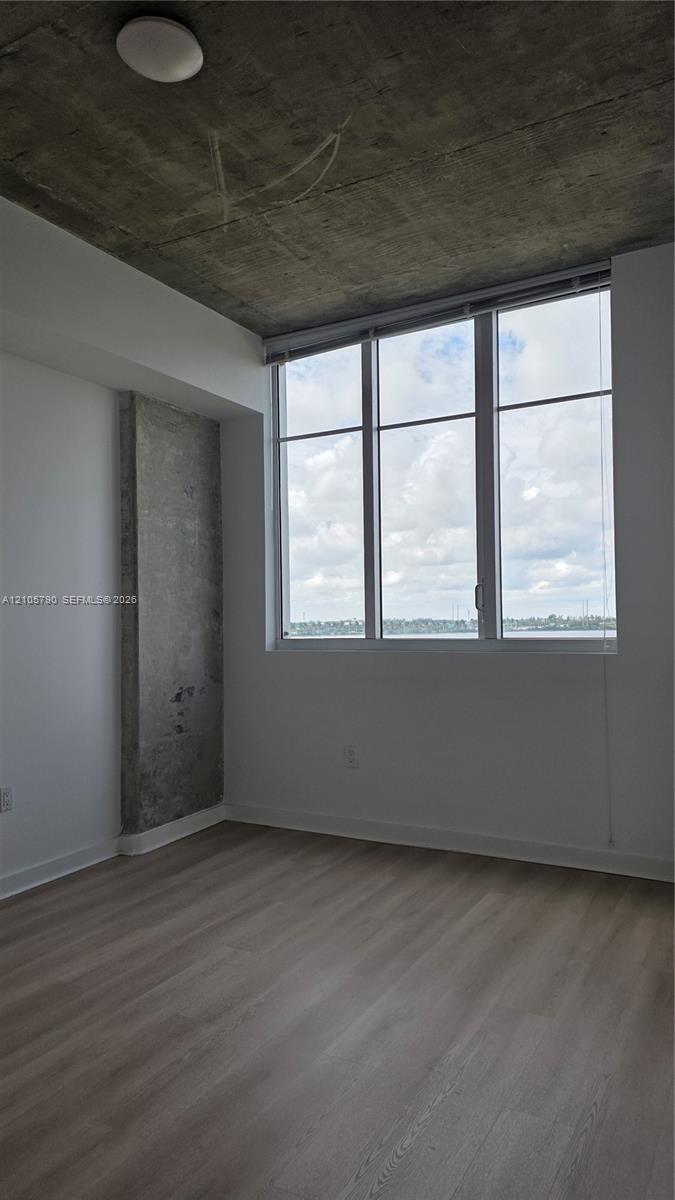 Exposed concrete ceiling and structural pillar, floor-to-ceiling windows, and wood-finish flooring