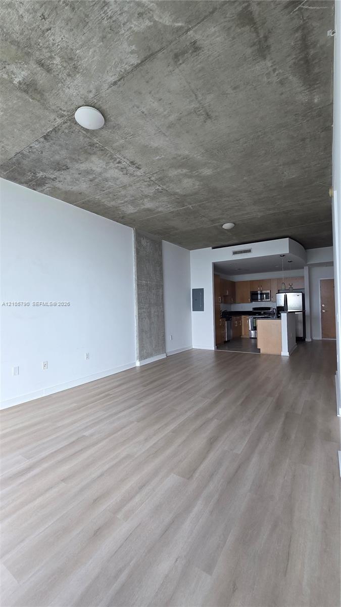 Exposed concrete ceiling, wood-finish flooring, and open-concept layout featuring a kitchen with stainless steel appliances and cabinetry