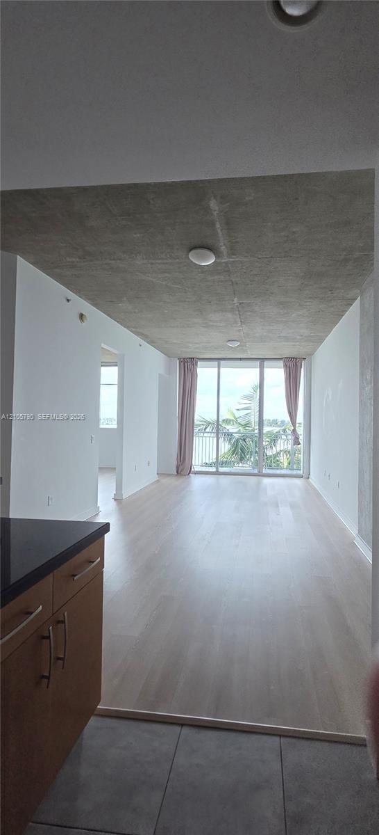 Exposed concrete ceiling, floor-to-ceiling glass doors, wood-finish flooring, and kitchen cabinetry featuring dark stone countertops