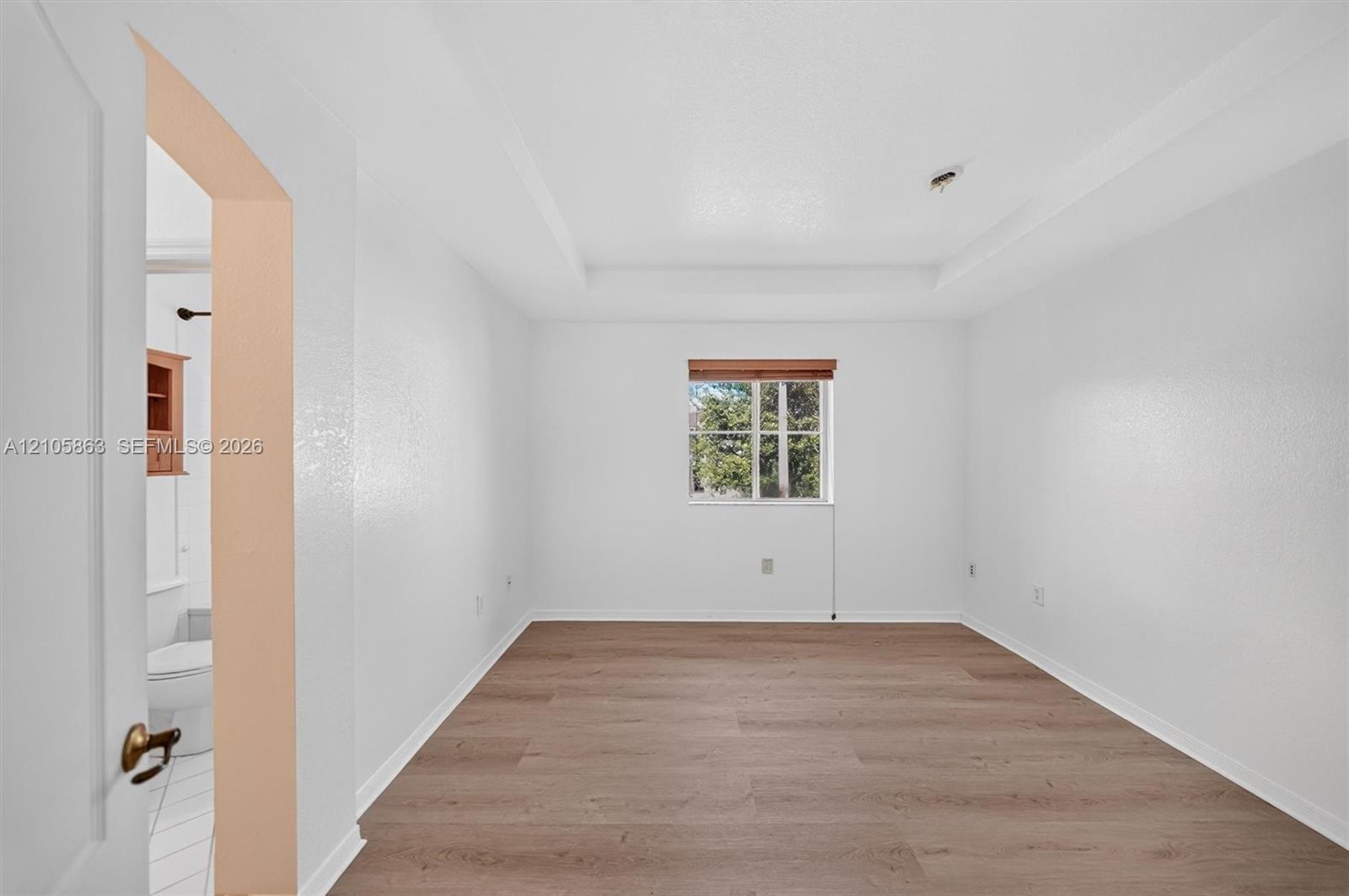 Tray ceiling, wood-finish flooring, and single-pane window with wood-trim framing