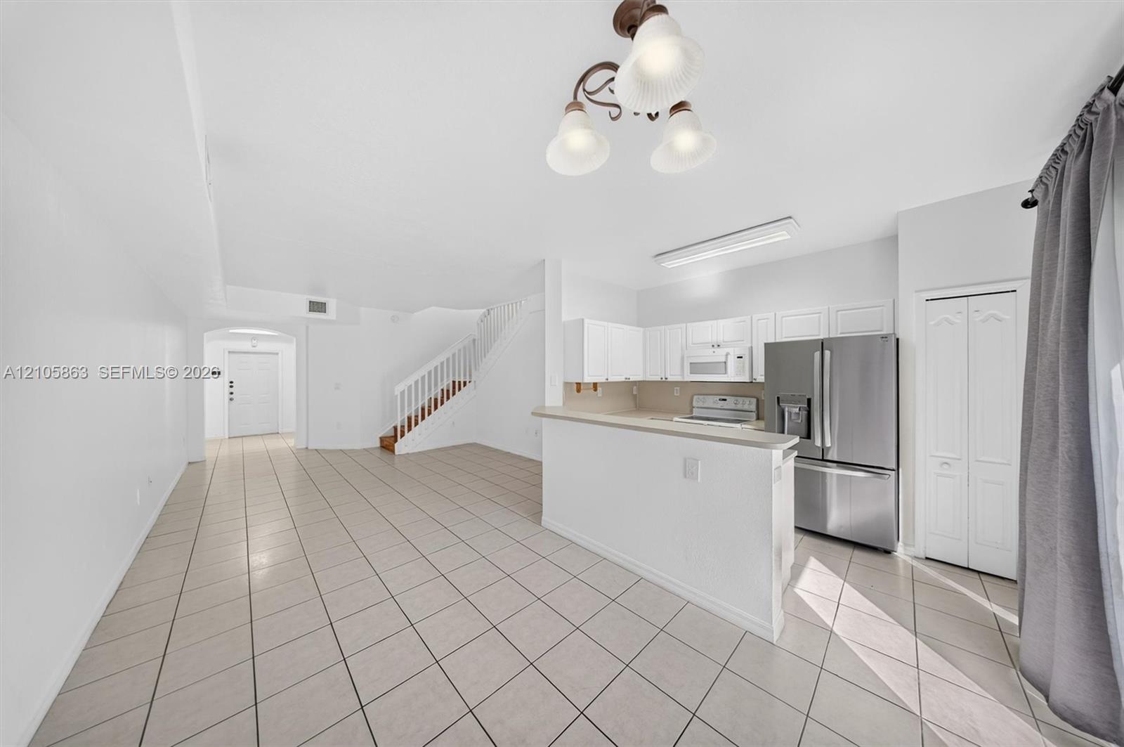 Kitchen featuring stainless steel appliances, white cabinetry, a breakfast bar, ceramic tile flooring, and a multi-light chandelier