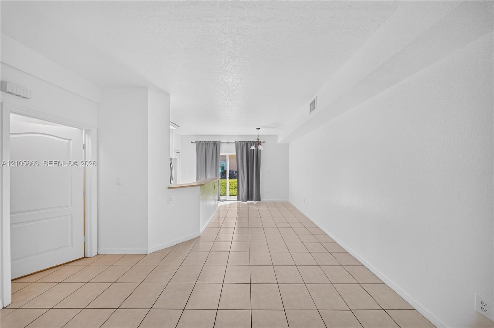 Neutral ceramic tile flooring, kitchen peninsula with a light-toned countertop, and sliding glass doors