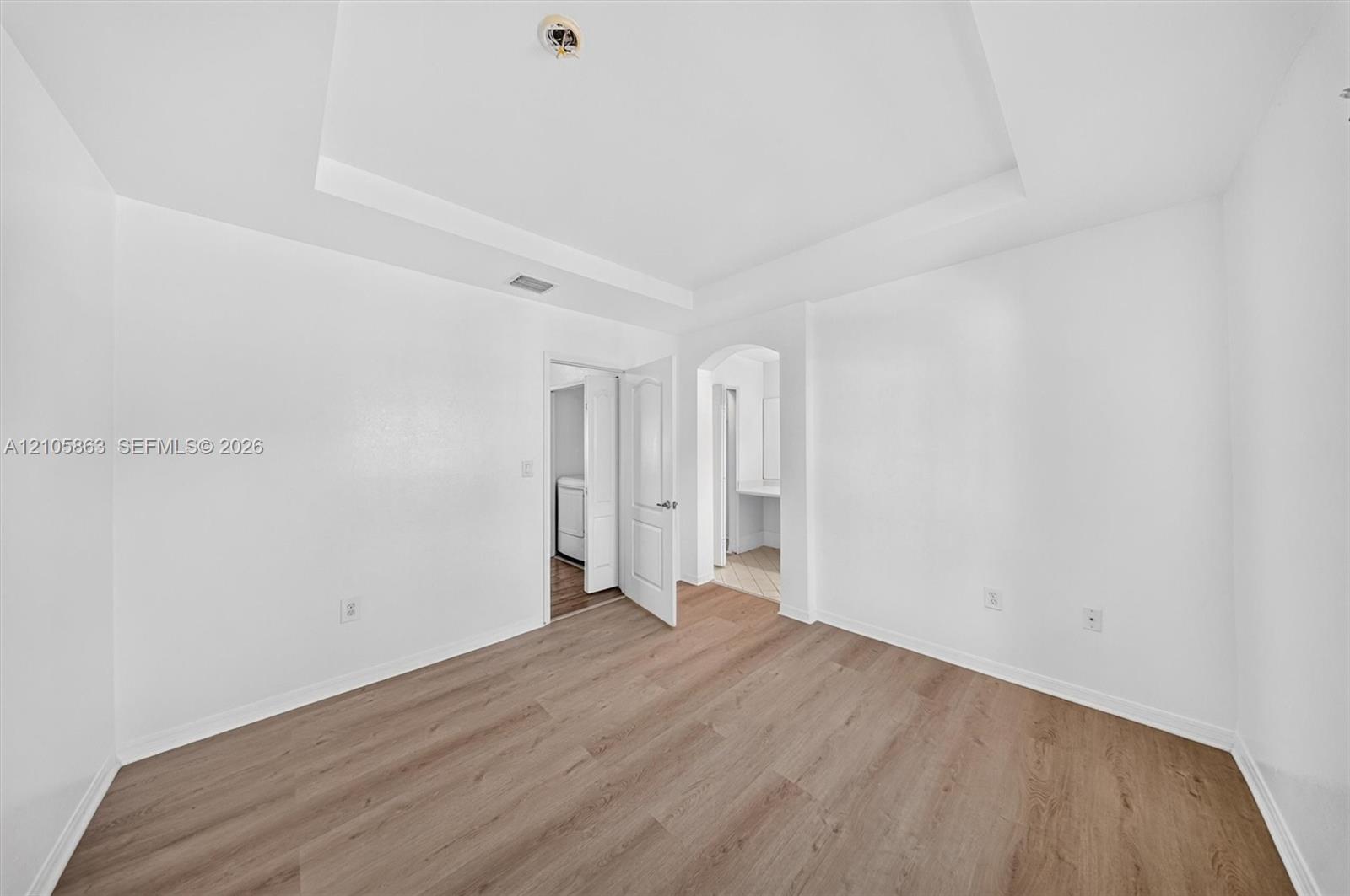 Interior space featuring a recessed tray ceiling, wood-finish flooring, and an arched entry