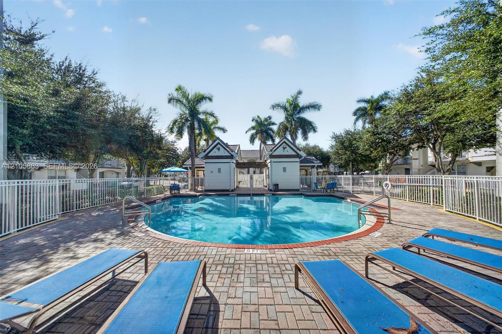 Swimming pool with circular basin, paver patio, white perimeter fencing, and dual cabana structures