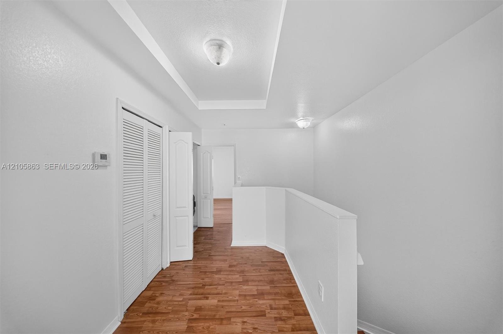 Tray ceiling with flush-mount lighting, wood-finish flooring, and white louvered-door closet