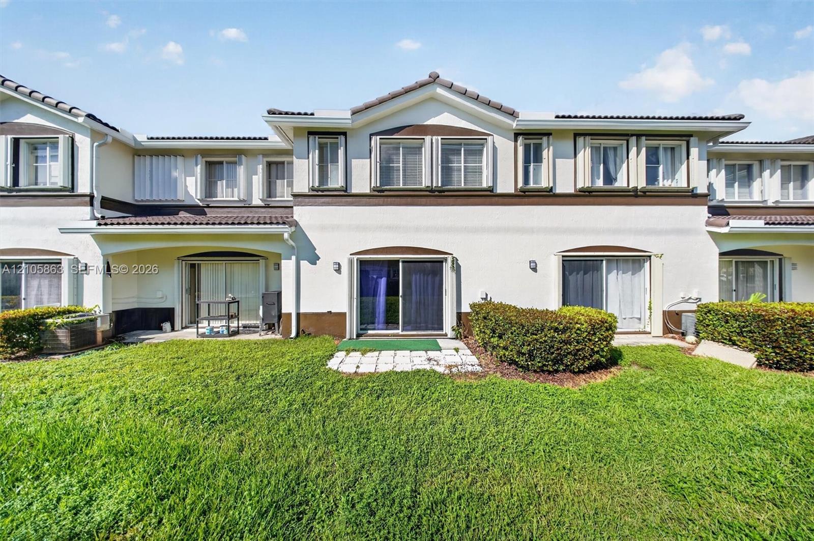 Stucco exterior featuring dual-tone trim, multi-pane windows, a tiled roofline, and sliding glass door access to a private lawn