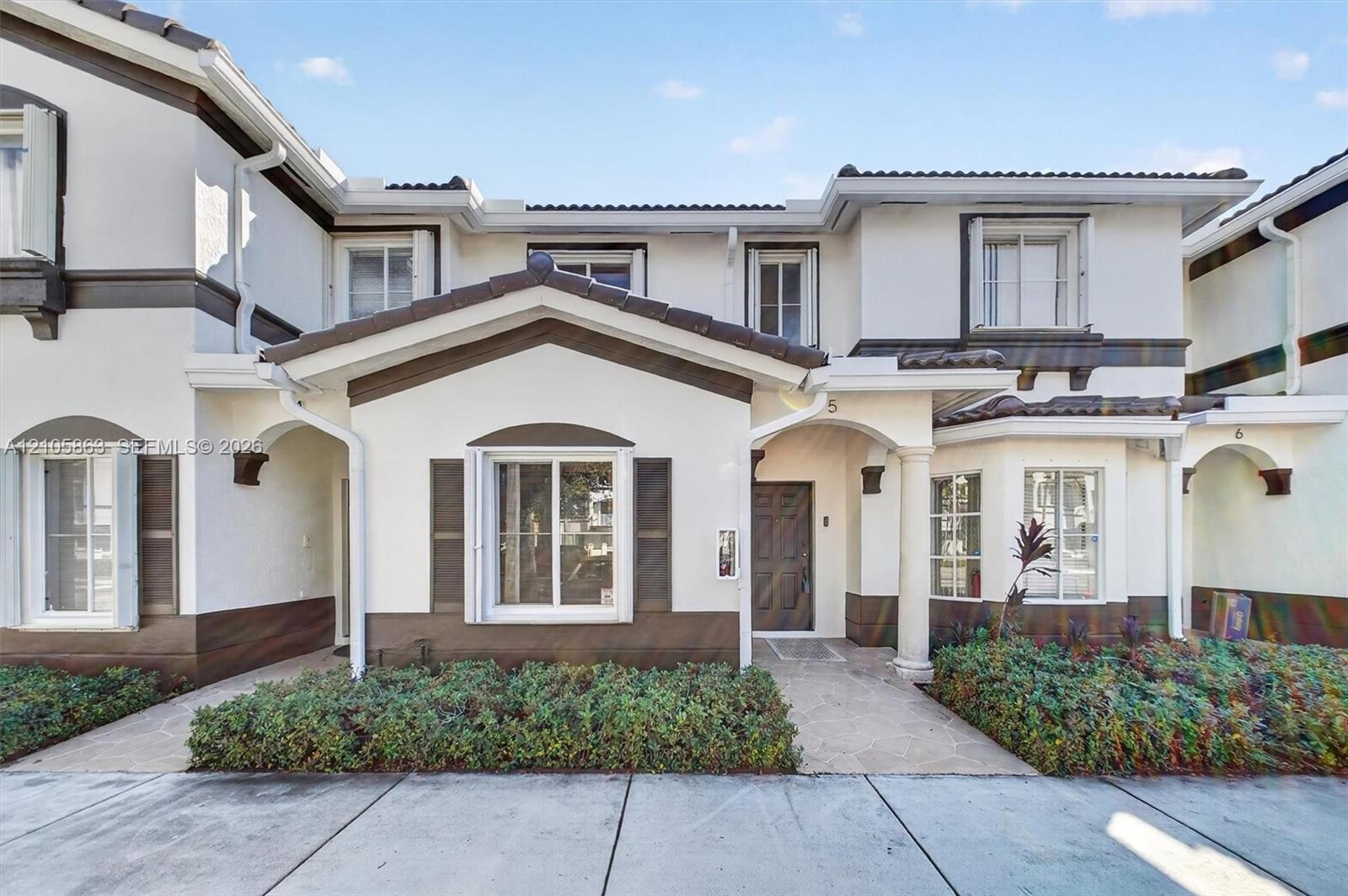 Two-story exterior featuring a light-toned stucco finish with contrasting dark trim, a covered entryway with a decorative pillar, and low-profile landscaping