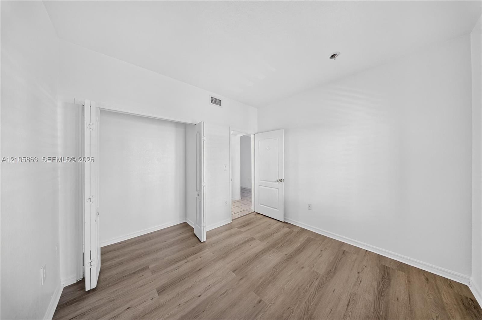 Room featuring wood-finish flooring, a multi-panel door, and a built-in closet with bi-fold doors
