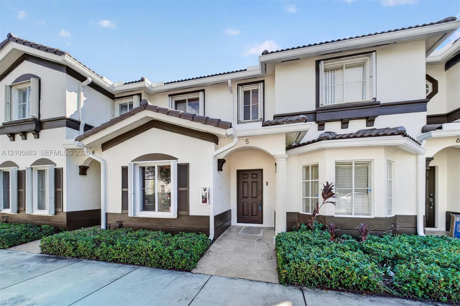 Two-story exterior featuring a light-toned stucco finish, dark wood-tone trim, a tiled roof, multi-pane windows, and a paved stone walkway