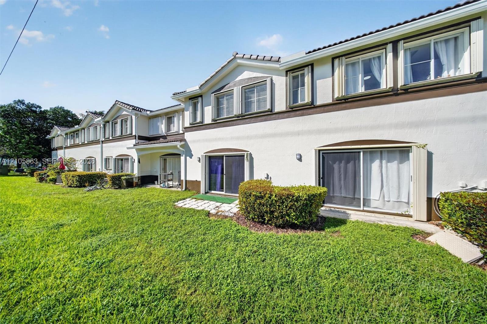 Stucco exterior featuring multi-gabled rooflines, stone-tiled patio accents, sliding glass door entryways, and expansive shared lawn space