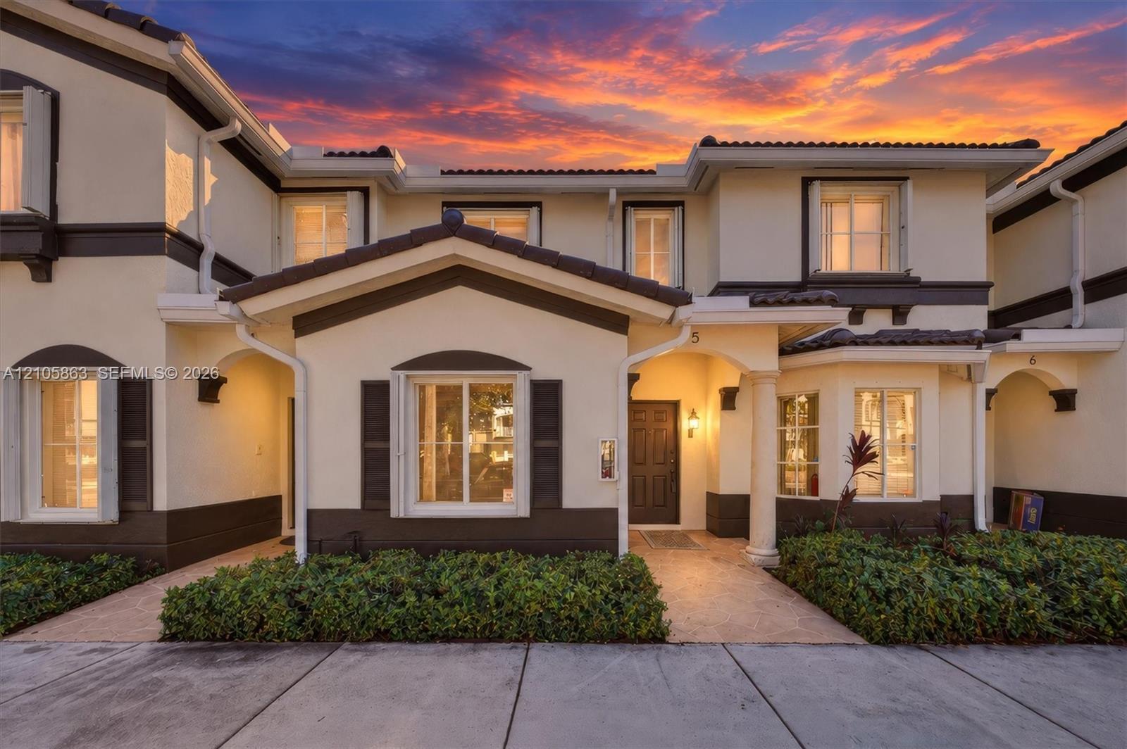 Two-story residence exterior featuring a high-contrast stucco facade, dark-toned trim, a covered entryway with a decorative column, and muntin-style windows