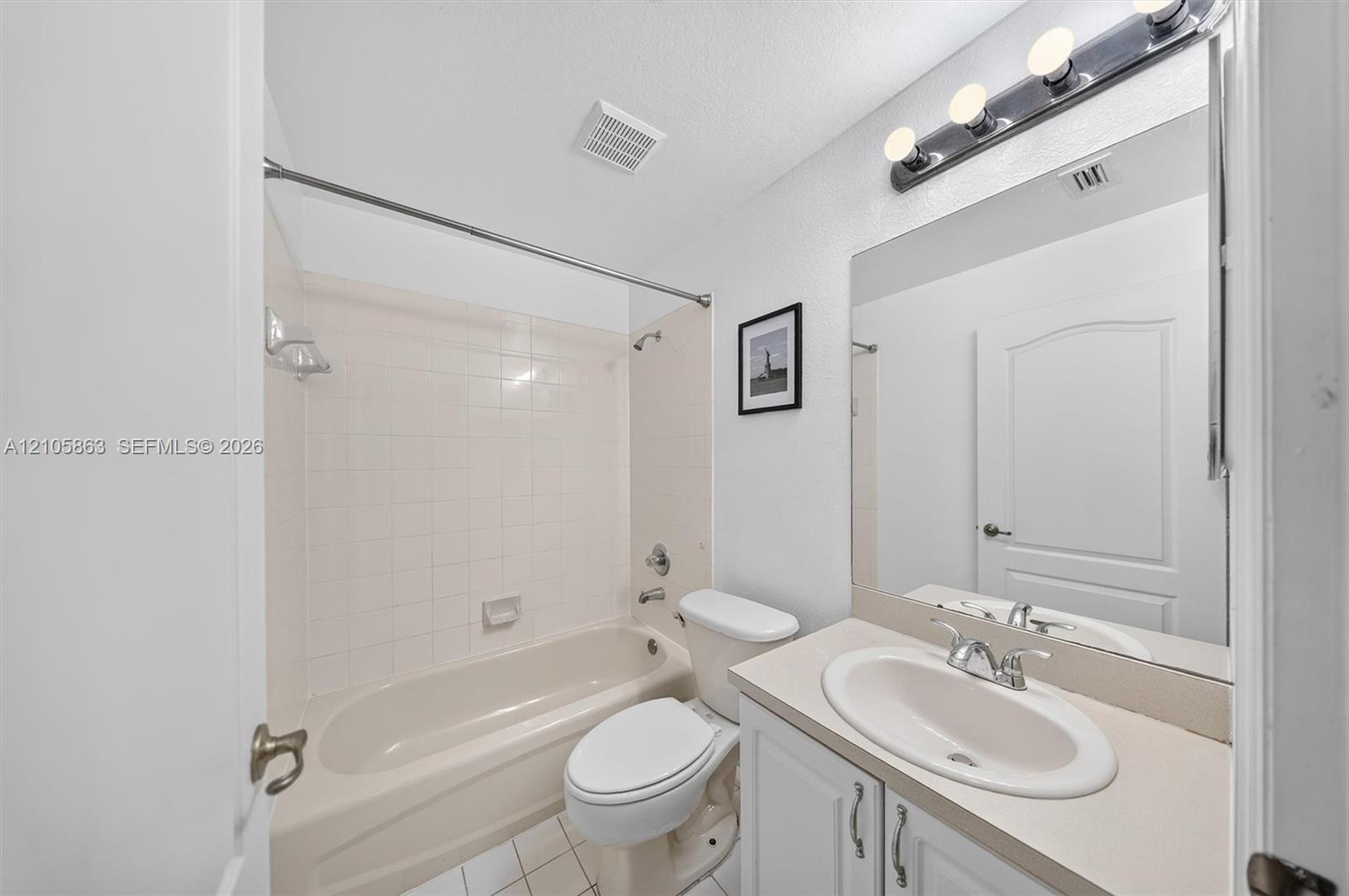 Full bathroom featuring a white vanity with a neutral solid-surface countertop, integrated oval sink, chrome dual-handle faucet, and an oversized wall mirror with a multi-bulb light fixture