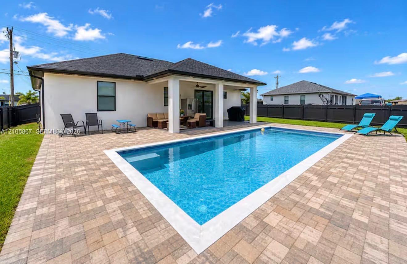 Stucco exterior with a covered patio, featuring an inground swimming pool surrounded by paved hardscaping and enclosed by a perimeter fence Stucco exterior with a covered patio, featuring an inground swimming pool surrounded by paved hardscaping and enclosed by a perimeter fence
