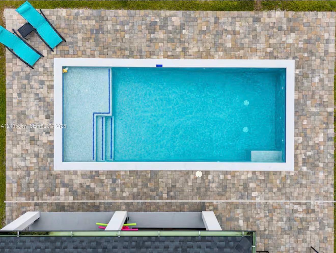 Rectangular swimming pool featuring a tiled interior, integrated entry steps, a built-in sun shelf, and a perimeter stone paver patio Rectangular swimming pool featuring a tiled interior, integrated entry steps, a built-in sun shelf, and a perimeter stone paver patio