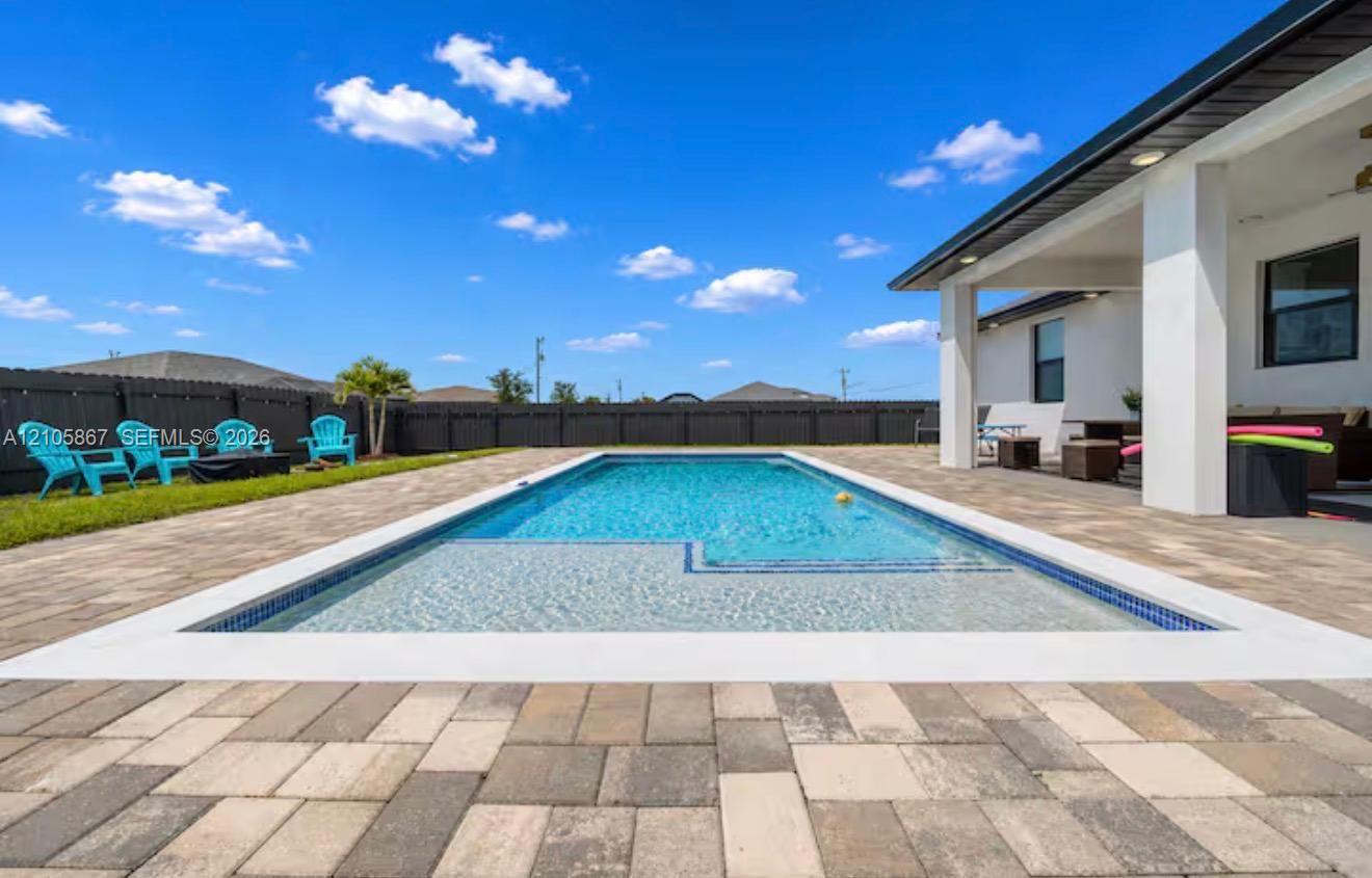 Rectangular in-ground pool featuring a shallow tanning ledge, surrounding paver patio, covered porch, and dark wood-tone privacy fencing Rectangular in-ground pool featuring a shallow tanning ledge, surrounding paver patio, covered porch, and dark wood-tone privacy fencing
