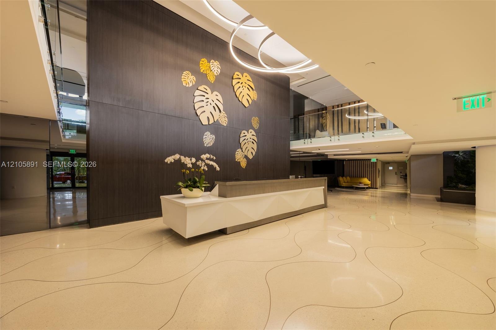 Lobby featuring high-gloss flooring with inlaid curvilinear detailing, a dark-finish wood-paneled accent wall with metallic leaf-shaped wall art, a structured white reception desk, and circular architectural light fixtures
