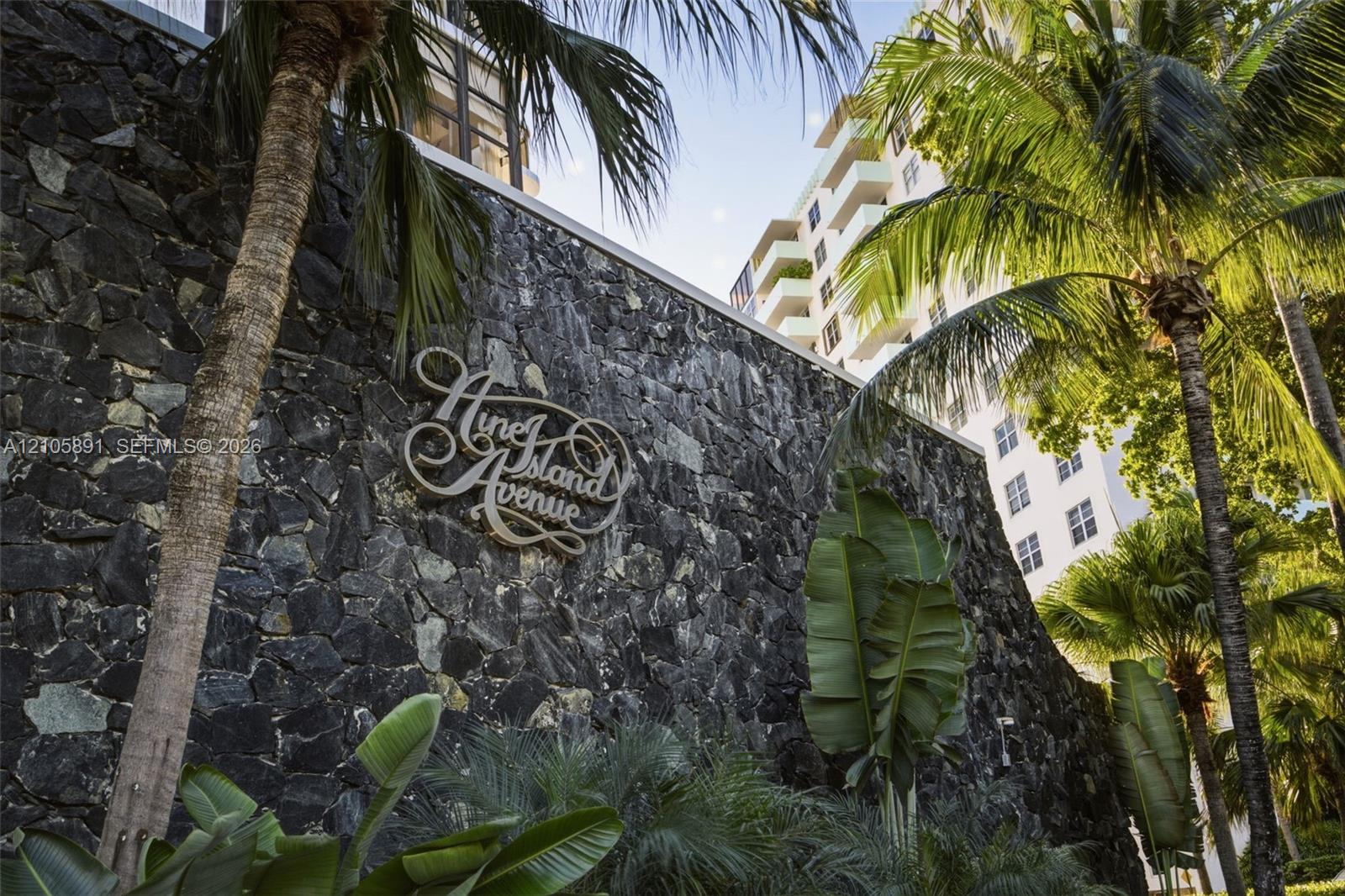 Natural stone masonry wall featuring custom metal signage, accented by mature palm trees and tropical landscaping
