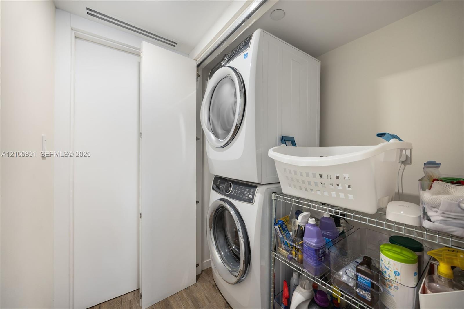 Laundry closet featuring a stacked washer and dryer unit, flat-panel door, and wood-finish flooring