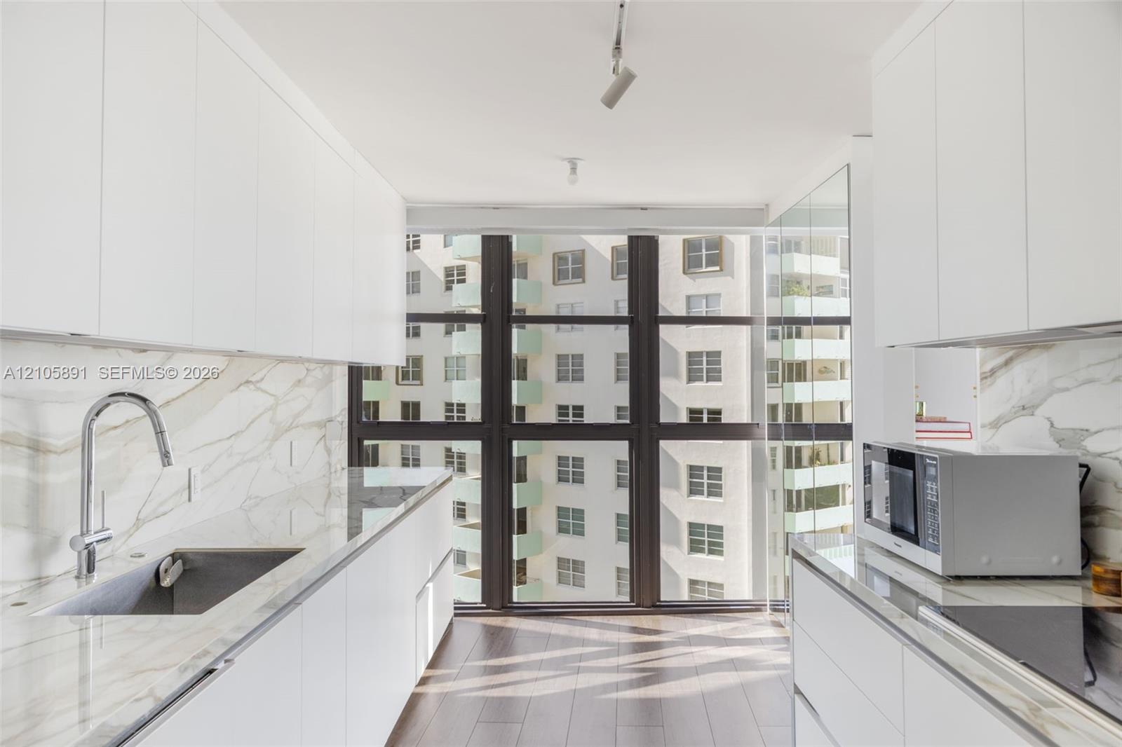 Kitchen featuring white flat-panel cabinetry, floor-to-ceiling windows, veined stone-finish countertops and backsplash, wood-finish flooring, and a stainless steel undermount sink with a gooseneck faucet