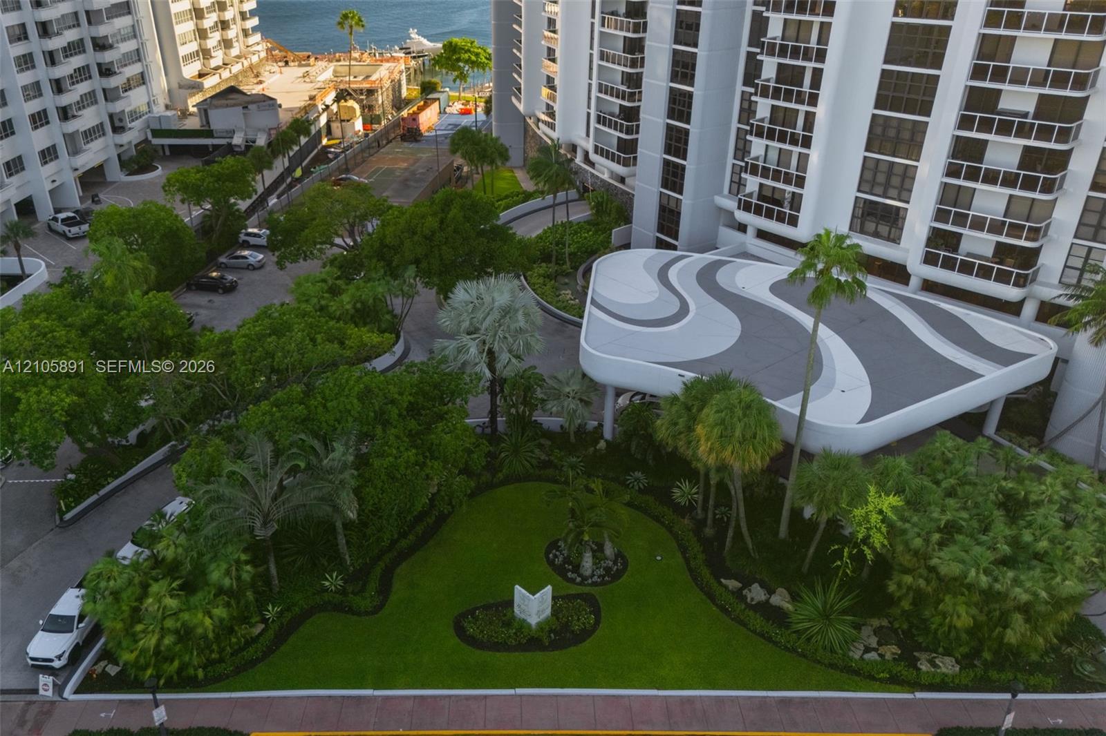 High-rise exterior featuring a patterned porte-cochre, manicured landscaping, mature trees, and paved motor court