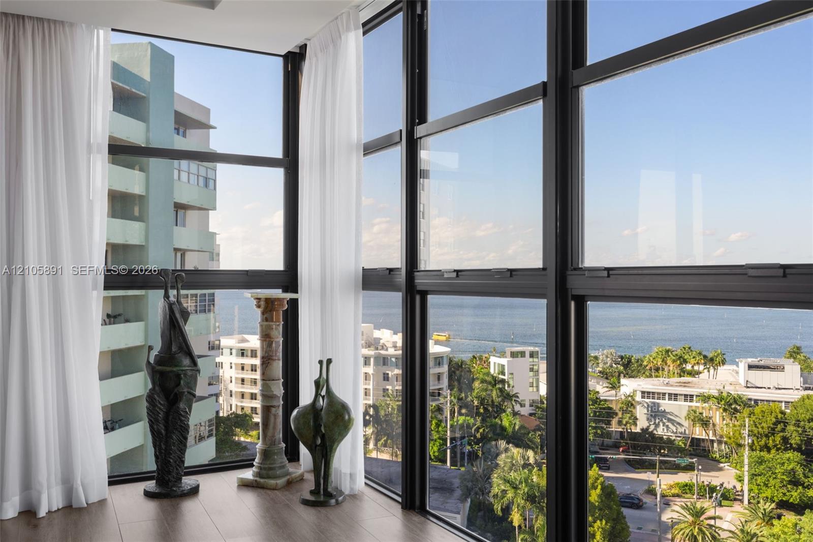 Floor-to-ceiling black metal-framed windows, wood-finish flooring, and coastal scenery