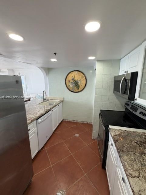 Kitchen featuring white cabinetry, stone-finish countertops, stainless steel appliances, ceramic tile flooring, and recessed lighting