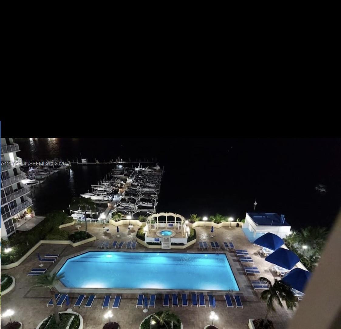 Swimming pool featuring an elevated spa with a decorative arched enclosure, stone-paver patio, and water frontage with private boat slips Swimming pool featuring an elevated spa with a decorative arched enclosure, stone-paver patio, and water frontage with private boat slips