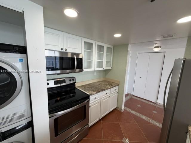 Kitchen featuring white cabinetry with glass-panel upper doors, stone-surface countertops, stainless steel appliances, and tiled flooring Kitchen featuring white cabinetry with glass-panel upper doors, stone-surface countertops, stainless steel appliances, and tiled flooring