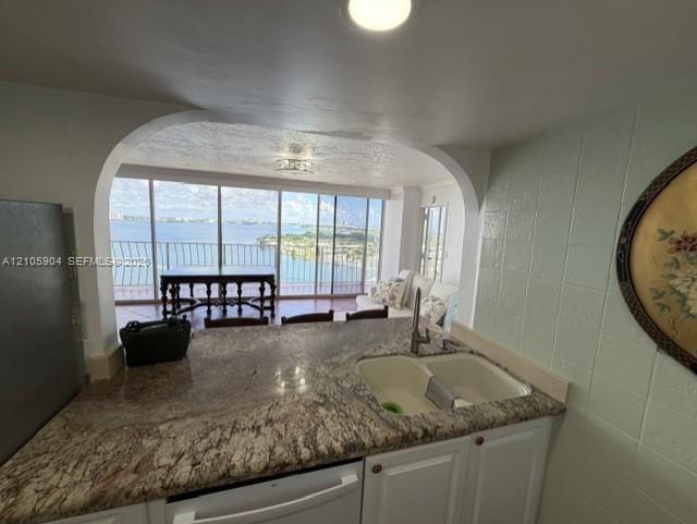 Kitchen featuring stone countertops, a dual-basin undermount sink, white cabinetry, and an arched pass-through opening to a balcony with water scenery Kitchen featuring stone countertops, a dual-basin undermount sink, white cabinetry, and an arched pass-through opening to a balcony with water scenery