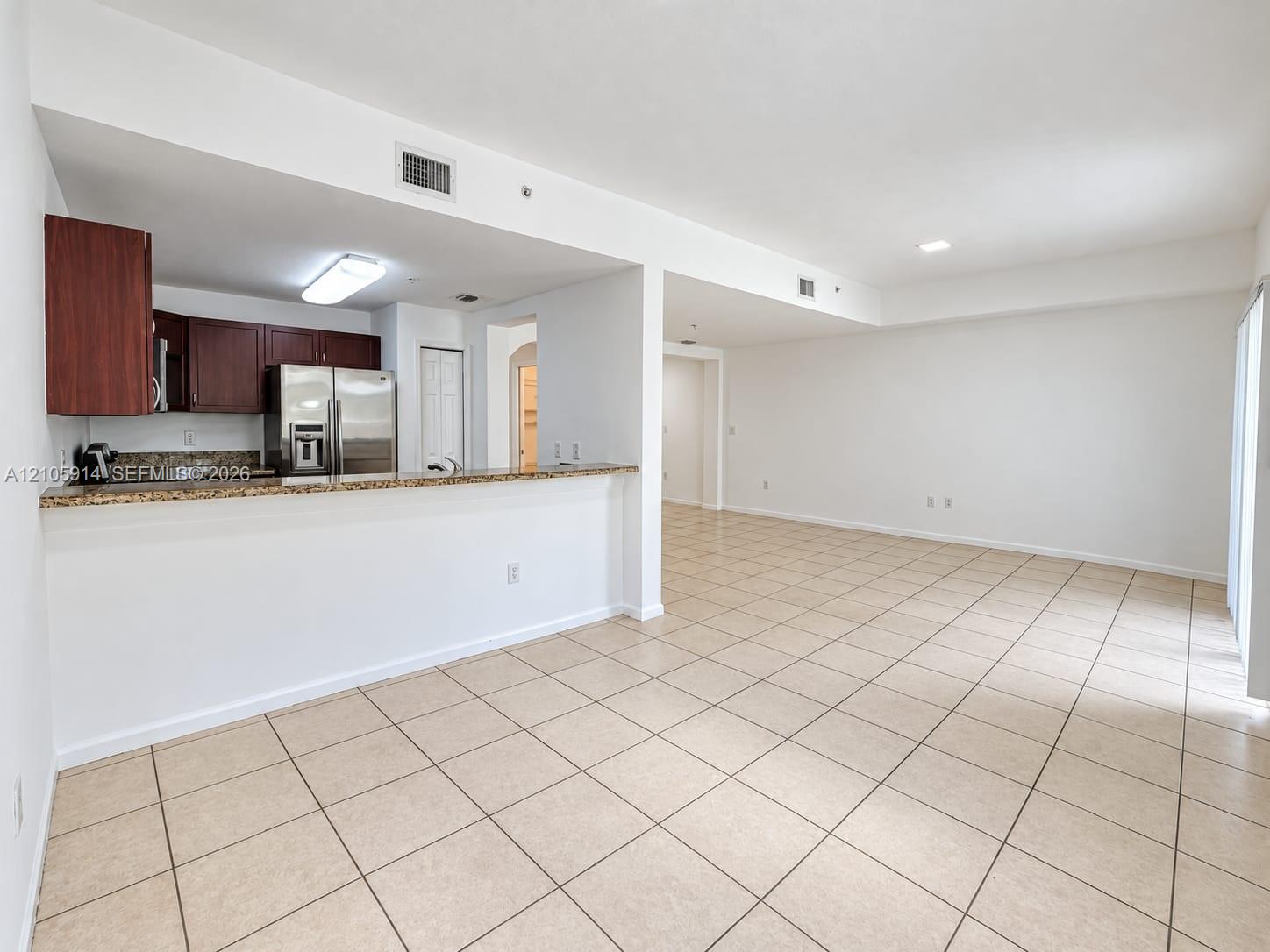 Kitchen featuring a breakfast bar with stone-finish countertops, dark wood cabinetry, and stainless steel refrigerator, complemented by neutral tile flooring throughout the interior