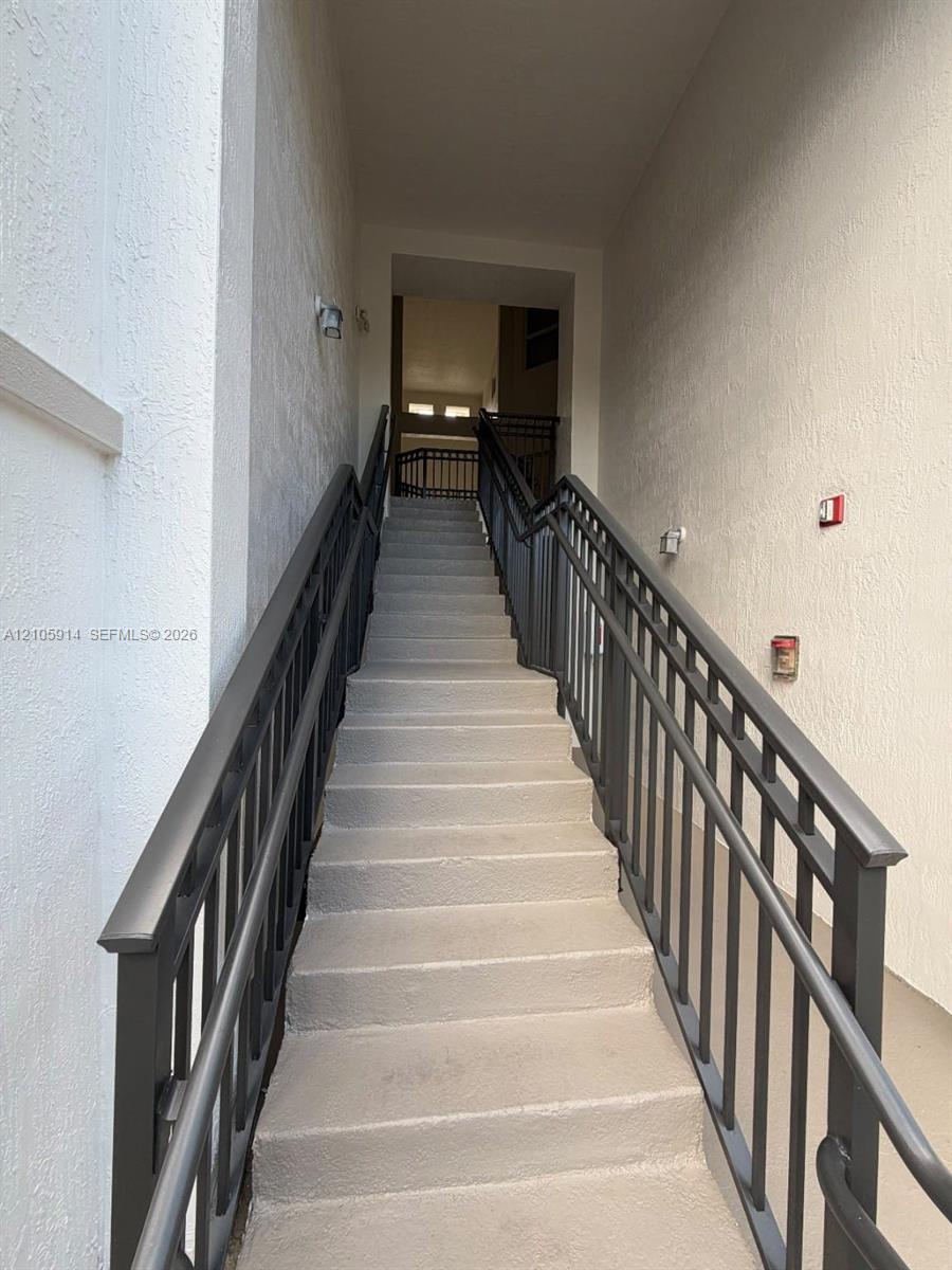 Staircase featuring concrete steps, dual dark-finish metal handrails, and textured wall surfaces